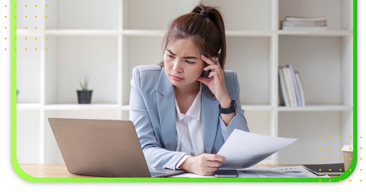 A confused lady in the office holding a paper and looking at her computer